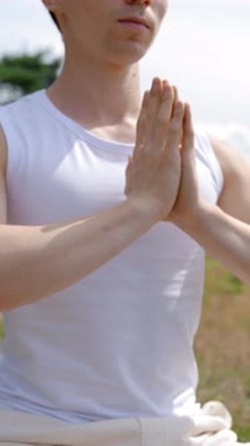 Vertical of Man Meditates in Lotus Pose Folding Hands on High Grass Hill