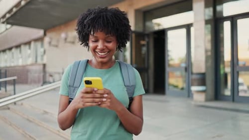 Smiling Woman Using Phone on College Campus