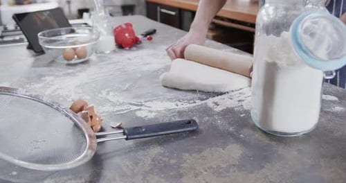 Hands of caucasian man preparing bread dough using tablet in kitchen, slow motion