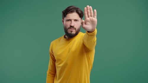 Man Makes Stop Gesture Against Green Background