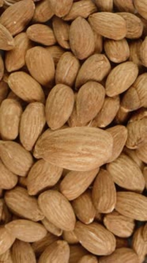 Vertical video. A solitary almond nut rotates against the backdrop of an immense pile of other nuts.