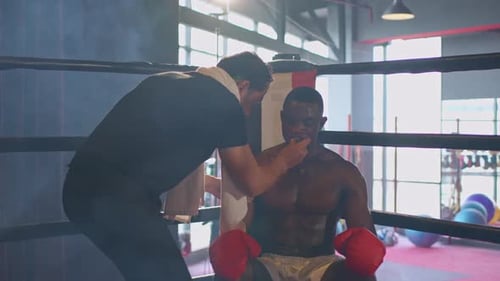 Asian fitness trainer support African sportsman doing boxing in gym.