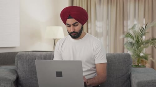 Homme indien sikh sérieux utilisant un ordinateur portable