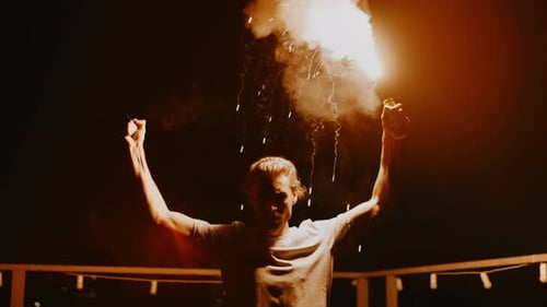 Man Waving Sparkler on Balcony at Night