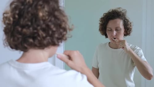 Woman Brushing Teeth in Bathroom Mirror