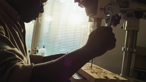 Carpenter Using Drill Press in Sunlit Woodworking Workshop