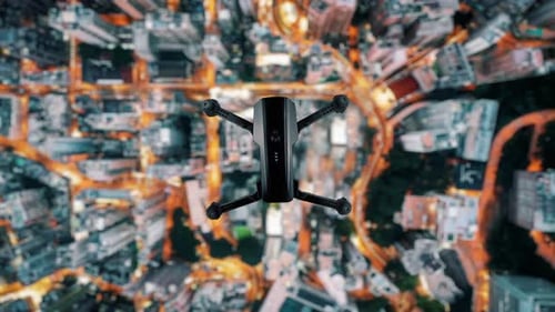 Drone Hovering Above Illuminated Modern City at Night