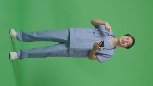Full Body Of Asian Male Doctor With Stethoscope Pointing To Smartphone In Hand On Green Screen