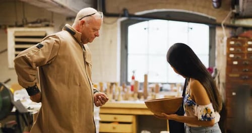 Man Showing Wooden Bowl to Woman in Workshop