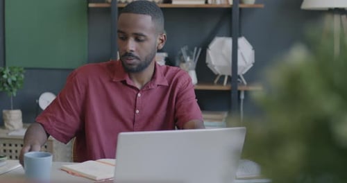 Ehrgeiziger Freiberufler, der am Laptop tippt und Tee aus einer Tasse trinkt, arbeitet am Schreibtisch im Büro