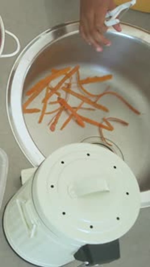 Vertical video: Entering hands in yellow tee and watch collecting carrot peels at sink for compost