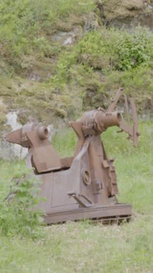 Vertical image of a rusted artillery mount abandoned in an overgrown grassy field.