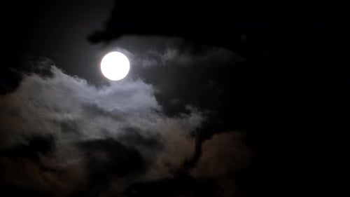 Bright round orb of full moon in dark night sky as clouds ominously pass by