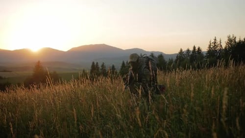 Camouflaged Figure Walking Through Grassy Field at Sunrise
