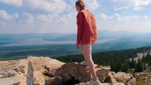 Young Woman Climbing on the Mountain and Raises Her Hands Up
