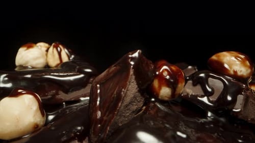 Close-up of a mound of chocolate squares and hazelnuts rotating on a black background.