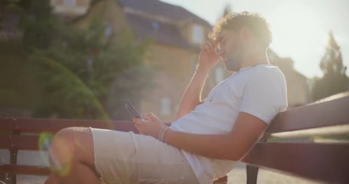 Man on Bench Looking at Phone on Sunny Day