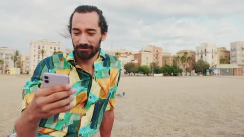 Young happy man using mobile phone on the beach