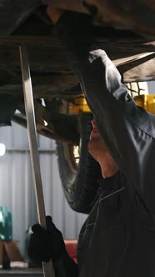 Mechanic in Car Service Checks the Auto's Bottom for