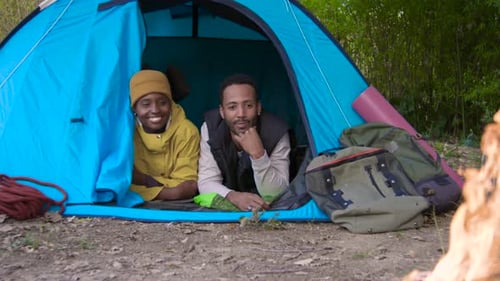 Glückliches schwarzes Paar genießt im Zelt beim Campen in der Natur am Lagerfeuer und hat gemeinsam Spaß