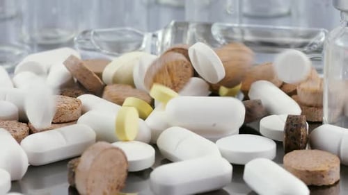 Falling tablets and pills on a metal surface on the background of glass bottles and ampoule.