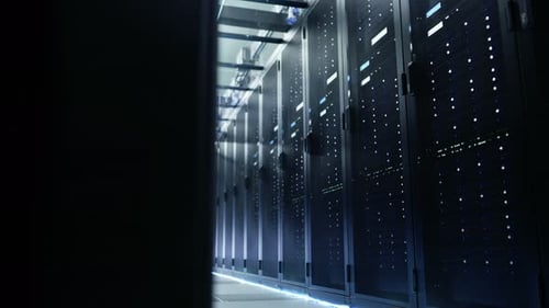 La caméra traverse un grand centre de données en activité avec des baies de serveurs et un plafond en verre.