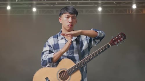 Adolescent asiatique avec guitare faisant un geste de temps mort avec les mains sur scène