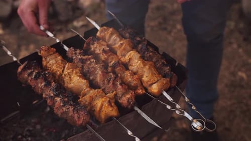 Männliches Handgrillen von Fleisch auf dem Außengrill. Fleischgrillen auf einem Holzkohlegrill beim Picknick.