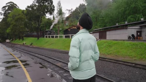 Rear Of An Indian Sikh Man Standing Near The Railway With Steam Train At Background. Medium Shot