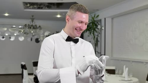 A Waiter in a White Shirt and Bow Tie Writes Down an Order and Laughs in the Restaurant