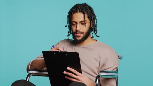 Man in Wheelchair Writing on Clipboard with Pen Studio Background
