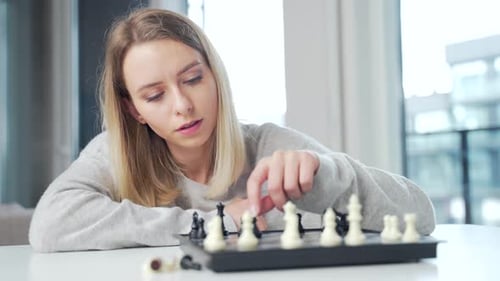 Portrait young attractive woman playing chess game online using laptop at home in the kitchen