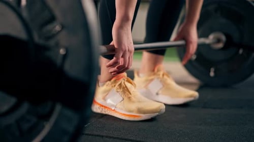 Closeup in the Gym Girl Trainer in Black Leggings is Going to Lift a Barbell with a Weight