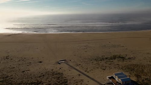 Aerial view of long beach, flying in direction of the ocean. Gentle waves with a beautiful sun refle