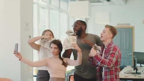 Happy business team celebrating success with money and taking selfies in the office