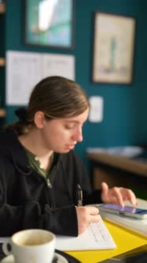 A Woman is Writing in a Notebook at a Desk in an Office She is Focused on Her Work