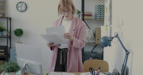 Portrait of Young Office Worker Reading Papers Standing at Desk Alone