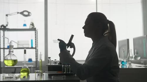 Side View of a Dark Silhouette of a Female Scientist Looking Under a Microscope Doing an Analysis of