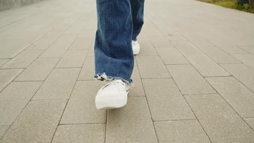 Junge Frau in blauen Jeans und weißen Turnschuhen läuft beim Sunny Day Closeup Walk auf der Asphaltstraße