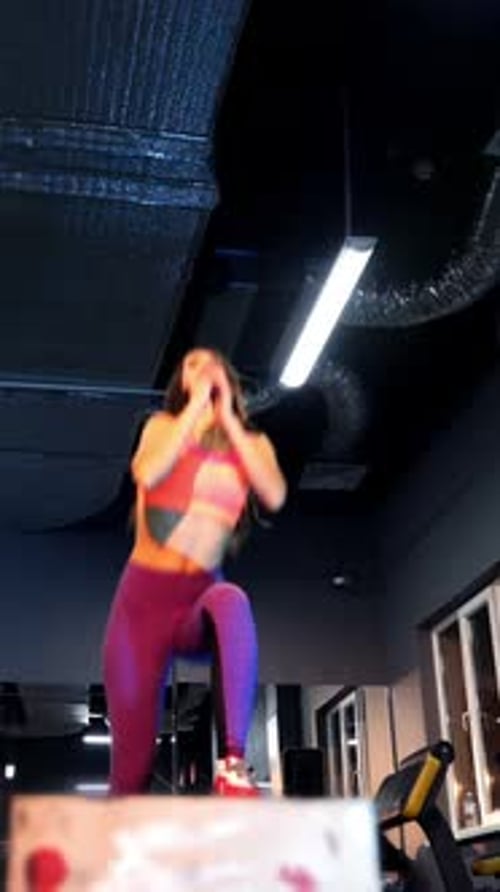 Attractive fitness woman in sportswear doing jumps on a big box in a training centre.