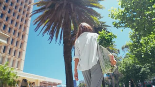 Una mujer con una bolsa ecológica de verduras en la ciudad