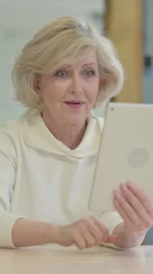 Excited Senior Woman Celebrating Success Using Tablet Indoors