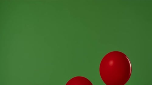 Two Red Helium Balloons with Shiny Ribbons Float Upward Against a Green Background with a Chroma Key