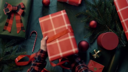 woman wrapping Christmas gifts on a table, with red boxes and a green tablecloth