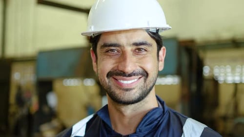 Confident male industrial worker or engineer wearing safety uniform smiling at the camera in factory