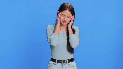 Young Woman Rubbing Temples Against Blue Backdrop