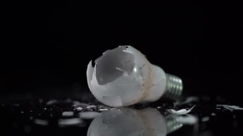 Incandescent tungsten light bulb of dusty lamp broken on glass pieces on black background