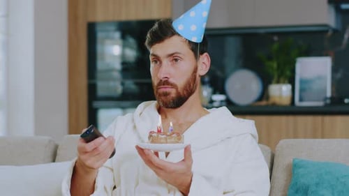 Close Up Young Man Celebrates Birthday Alone Hold Cake Watch TV Sitting at Sofa in the Living Room