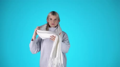 Stylish Young Blonde Woman, Adjusting Scarf and Wearing Grey Sweater, Studio Shot With Blue Backgrou