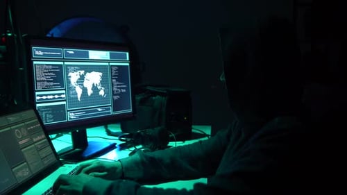 Hooded Hacker Working on Computers in Dark Room